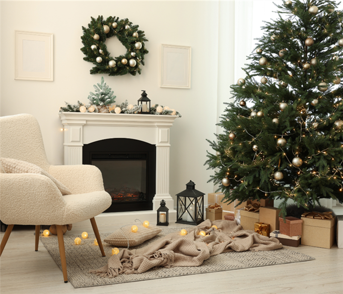 A cozy photo of a living room filled with Christmas decorations, a lit fireplace with a wreath above it, and an xmas tree. 